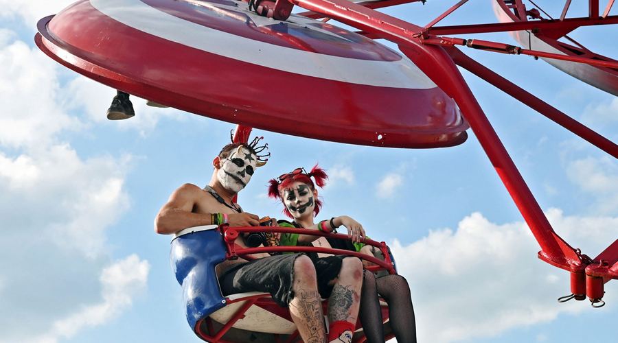 A juggalo and juggalette couple in clown face paint and spiked hair share a ride on a tilt-a-whirl at the 2023 Gathering of the Jaggalos music festival